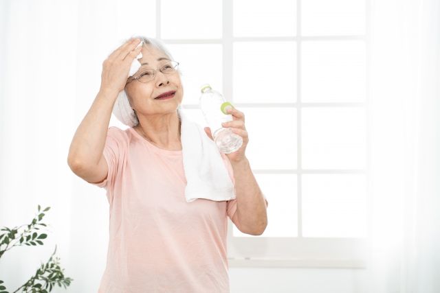 汗を拭いて水分補給する高齢女性.jpg